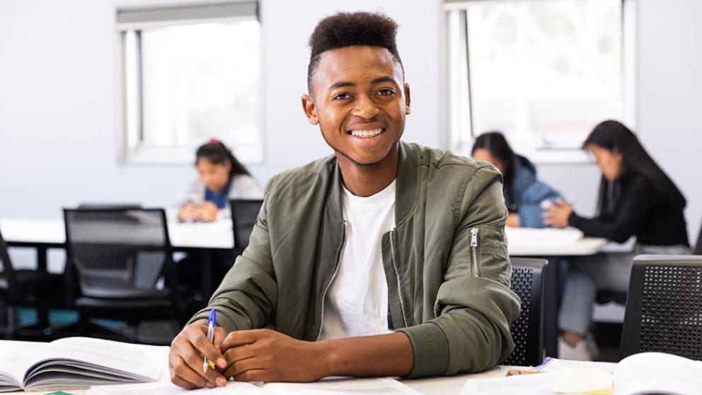 Benjamin smiling widely as he sits in class, his work on the desk in front of him