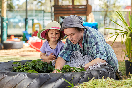 Justen, a VU graduate, with a young girl in the childcare centre, the two intently gardening in a herb patch.