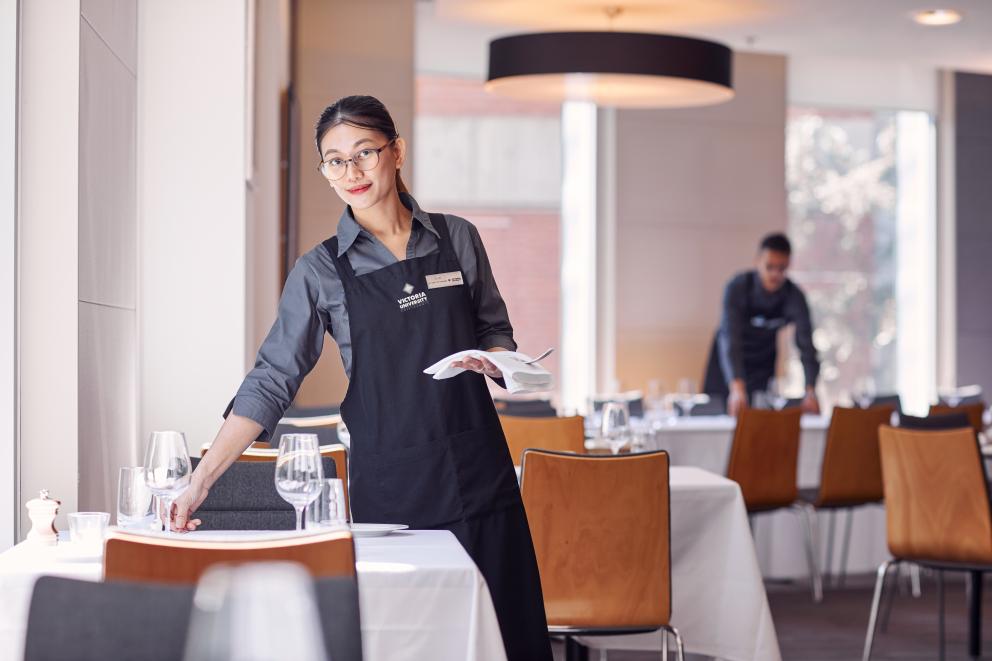 A hospitality student preparing a restaurant table prior to service beginning.